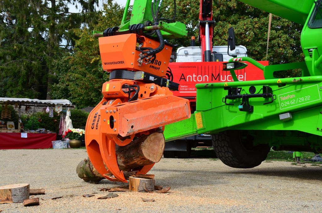 Anbaugerät mit Greifer und Schnittkopf aus der Nähe, dahinter der rote LKW mit Ladekran.