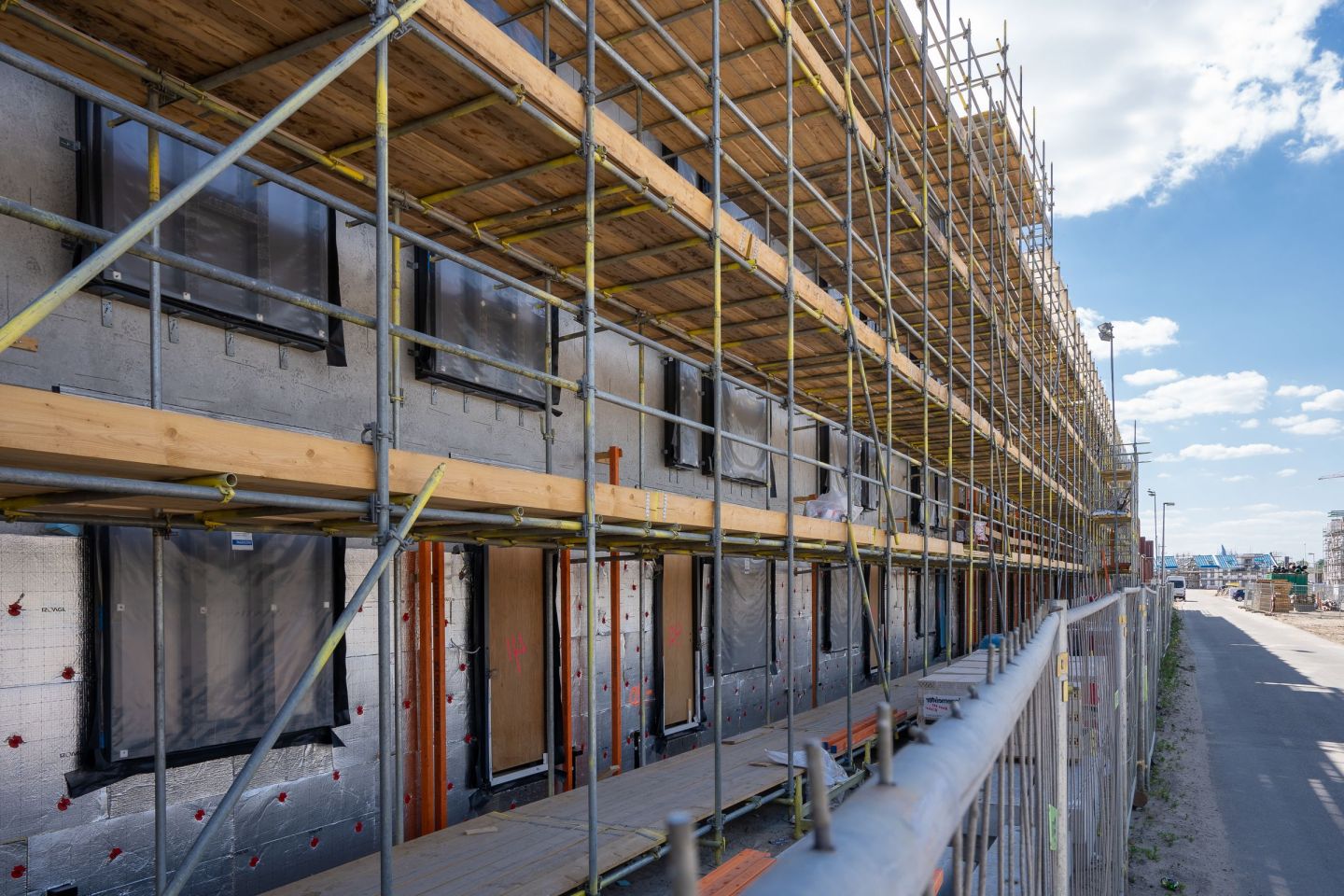 Fassadengerüst an einem Neubau, Beläge aus Holz, Lage über Lage, unter blauem Himmel.